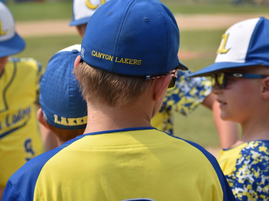 Canyon Lakers players close together, the club name stitched on a cap