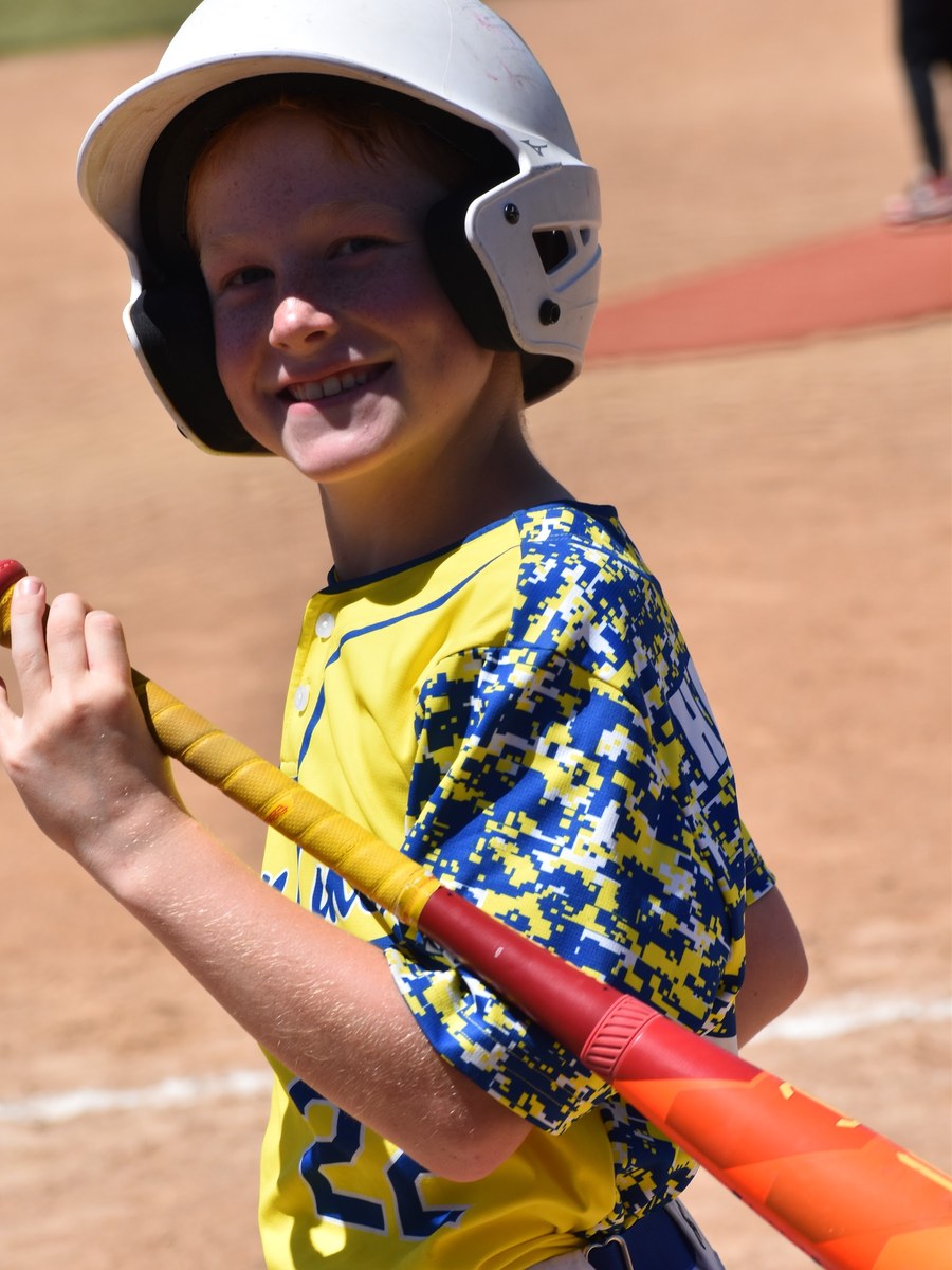 A grinning Canyon Lakers hitter waiting on deck with his bat